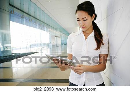 Stock Image - Mixed race businesswoman using tablet computer in lobby. Fotosearch