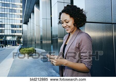 Stock Photography - Mixed race businesswoman using tablet computer in city. Fotosearch