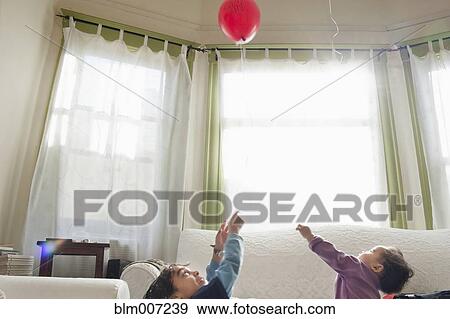 Mixed race children playing with balloon in living room View Large Photo Image Stock Photo - Mixed race children playing with balloon in living room. Fotosearch