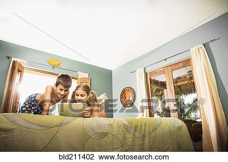 Stock Image - Mixed race children using digital tablet on bed. Fotosearch