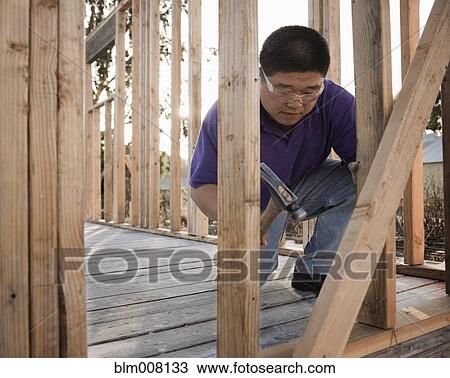 Mixed race construction worker using hammer on house frame View Large Photo Image Stock Image - Mixed race construction worker using hammer on house frame. Fotosearch