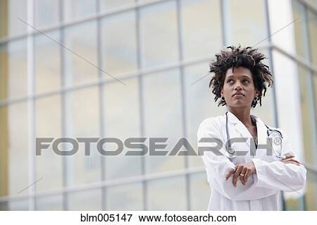 Stock Photo - Mixed race doctor standing outdoors with arms crossed. Fotosearch