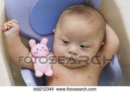 Picture - Mixed race Down Syndrome baby laying in plastic bathtub. Fotosearch