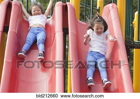 Stock Image - Mixed race Down syndrome girls playing on slides. Fotosearch