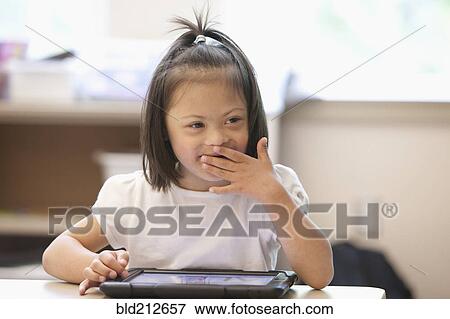 Stock Photo - Mixed race Down syndrome student using tablet computer in classroom. Fotosearch