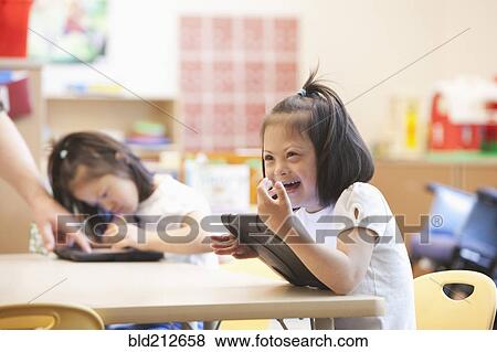 Stock Photo - Mixed race Down syndrome student using tablet computer in classroom. Fotosearch