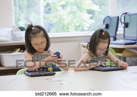 Stock Photograph - Mixed race Down syndrome students using tablet computers in classroom. Fotosearch