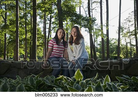 Mixed race friends sitting on stone wall View Large Photo Image Stock Image - Mixed race friends sitting on stone wall. Fotosearch