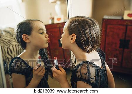 Stock Photo - Mixed race girl applying lipstick in mirror. Fotosearch
