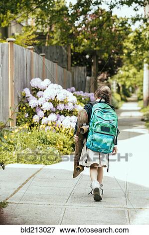 Stock Photo - Mixed race girl carrying skateboard on sidewalk. Fotosearch