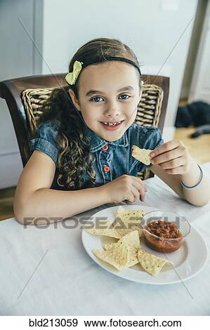 Stock Photo - Mixed race girl eating chips and salsa at table. Fotosearch