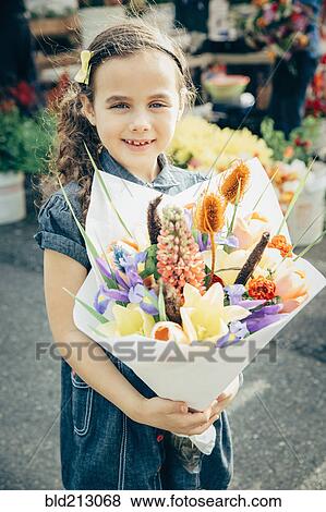 Stock Photo - Mixed race girl holding bouquet of flowers outdoors. Fotosearch