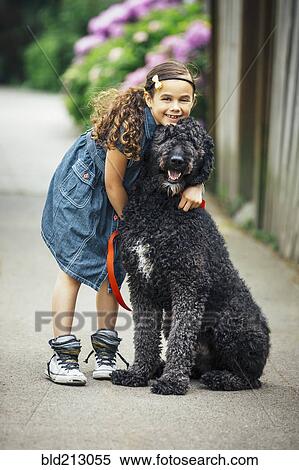 Stock Photography - Mixed race girl hugging dog on suburban sidewalk. Fotosearch