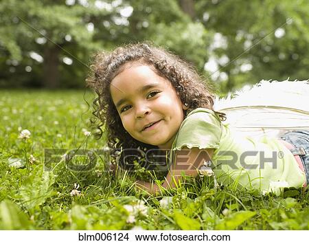 Picture - Mixed race girl laying in grass. Fotosearch