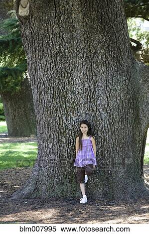 Stock Photography - Mixed race girl leaning against tree trunk in park. Fotosearch