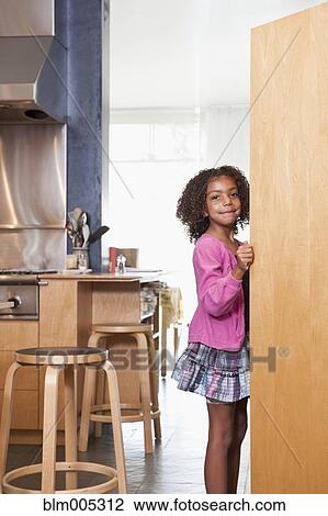 Stock Image - Mixed race girl opening kitchen cupboard. Fotosearch