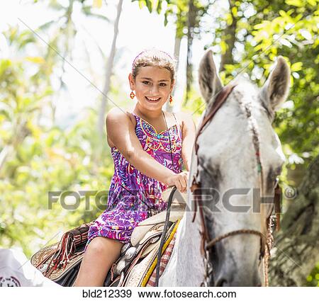 Stock Photo - Mixed race girl riding horse in jungle. Fotosearch