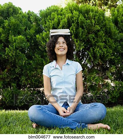 Mixed race girl sitting in grass balancing book on head View Large Photo Image Stock Photo - Mixed race girl sitting in grass balancing book on head. Fotosearch