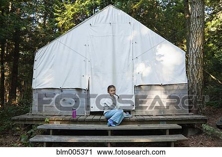 Stock Image - Mixed race girl sitting near tent. Fotosearch
