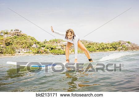 Stock Image - Mixed race girl surfing in waves. Fotosearch