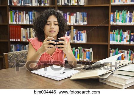 Stock Photograph - Mixed race girl text messaging on cell phone in library. Fotosearch
