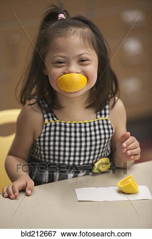Stock Photo - Mixed race girl with Down syndrome eating fruit. Fotosearch