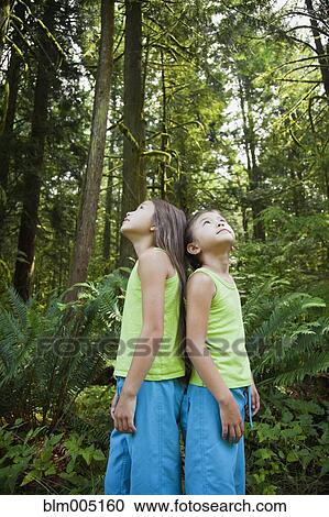 Stock Image - Mixed race girls standing back to back in forest. Fotosearch