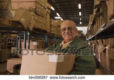 Stock Photo - Mixed race man carrying box in warehouse. Fotosearch
