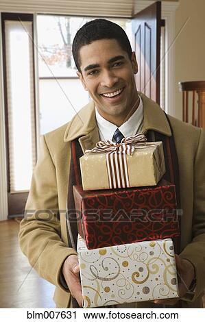 Stock Image - Mixed race man carrying stack of Christmas gifts. Fotosearch