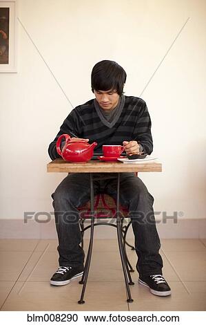 Stock Image - Mixed race man drinking tea and using digital tablet at cafe. Fotosearch