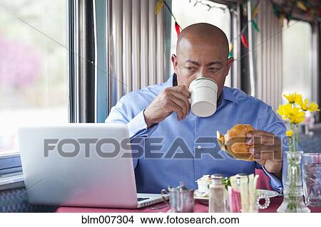 Mixed race man eating in diner and using laptop View Large Photo Image Picture - Mixed race man eating in diner and using laptop. Fotosearch