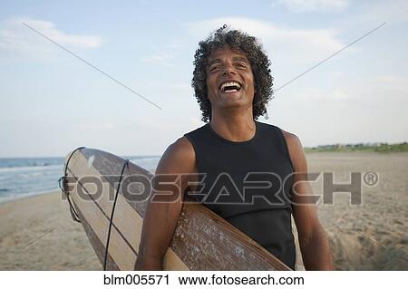 Mixed race man holding surfboard on beach View Large Photo Image Stock Image - Mixed race man holding surfboard on beach. Fotosearch