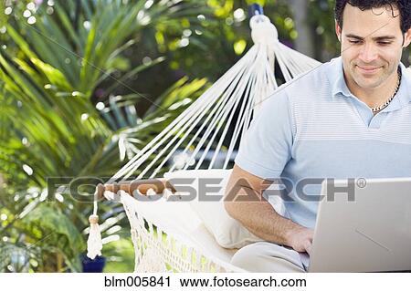 Stock Image - Mixed race man in hammock using laptop. Fotosearch