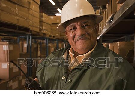Stock Photography - Mixed race man in hard-hat in warehouse. Fotosearch