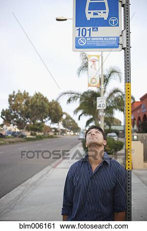 Stock Image - Mixed race man looking at bus stop sign. Fotosearch