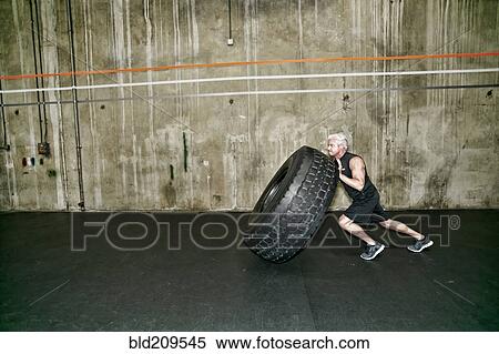 Stock Photography - Mixed race man pushing large tire in gym. Fotosearch