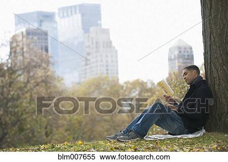 Stock Photography - Mixed race man reading book in park. Fotosearch