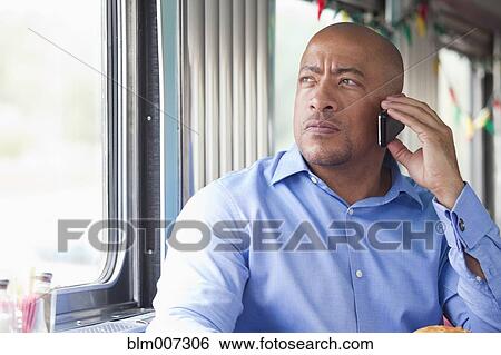 Stock Photograph - Mixed race man sitting in diner using cell phone. Fotosearch