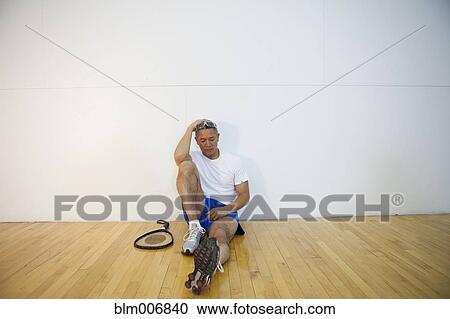 Stock Image - Mixed race man sitting in racquetball court. Fotosearch