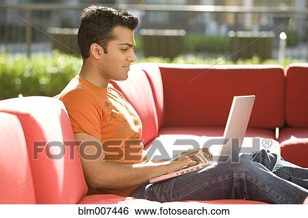 Mixed race man sitting on sofa and using laptop View Large Photo Image Stock Photograph - Mixed race man sitting on sofa and using laptop. Fotosearch