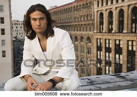 Stock Photo - Mixed race man sitting on urban rooftop. Fotosearch