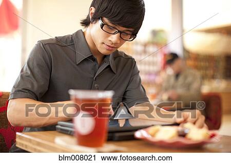 Stock Image - Mixed race man using digital tablet in cafe. Fotosearch