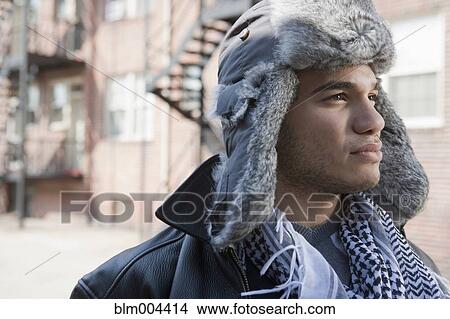 Picture - Mixed race man wearing fur hat and looking pensive. Fotosearch