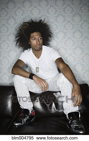 Stock Photography - Mixed race man with afro sitting on back of sofa. Fotosearch