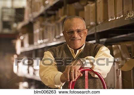 Stock Image - Mixed race man with hand truck in warehouse. Fotosearch