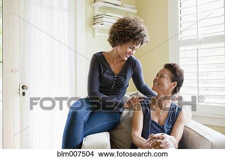 Picture - Mixed race mother and daughter sitting in armchair. Fotosearch