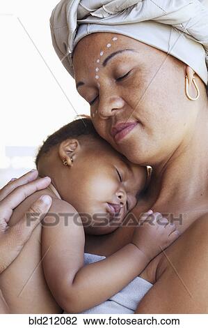 Stock Image - Mixed race mother cradling baby. Fotosearch