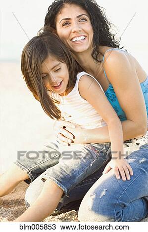 Stock Image - Mixed race mother holding daughter in lap. Fotosearch
