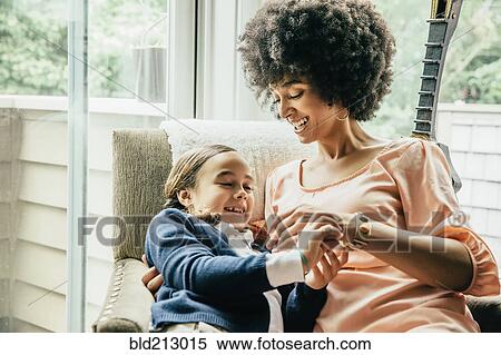 Stock Photography - Mixed race mother holding daughter in armchair. Fotosearch