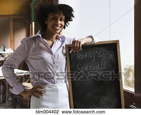Stock Image - Mixed race server leaning against blackboard with text ÆToday's SpecialsÆ. Fotosearch